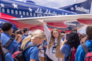 A girl poses for a photo in front of a red, white and blue airplane amid a throng of youths